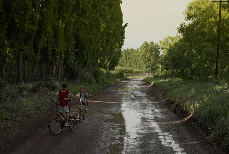 dos jovenes caminan junto a sus bicicletas a traves de una ruta de barro en el campo