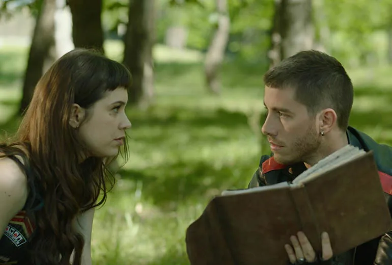 dos jovenes de diferentes sexos sentados en un campo con un libro en la mano